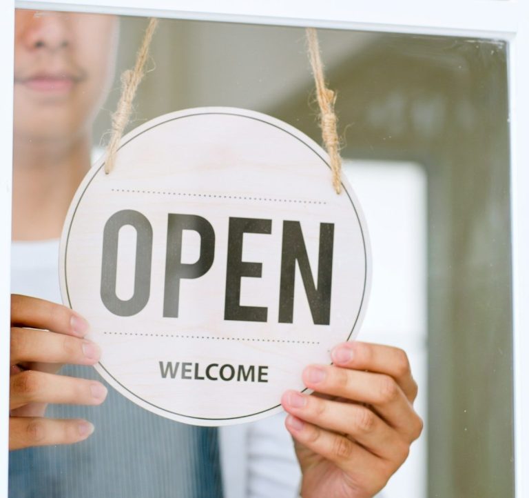 Person hält ein offenes Schild mit der Aufschrift „OPEN WELCOME“.